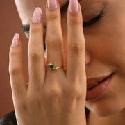 Close-up of a hand wearing a 14k gold filled ring with a green Emerald gemstone, held near the face.